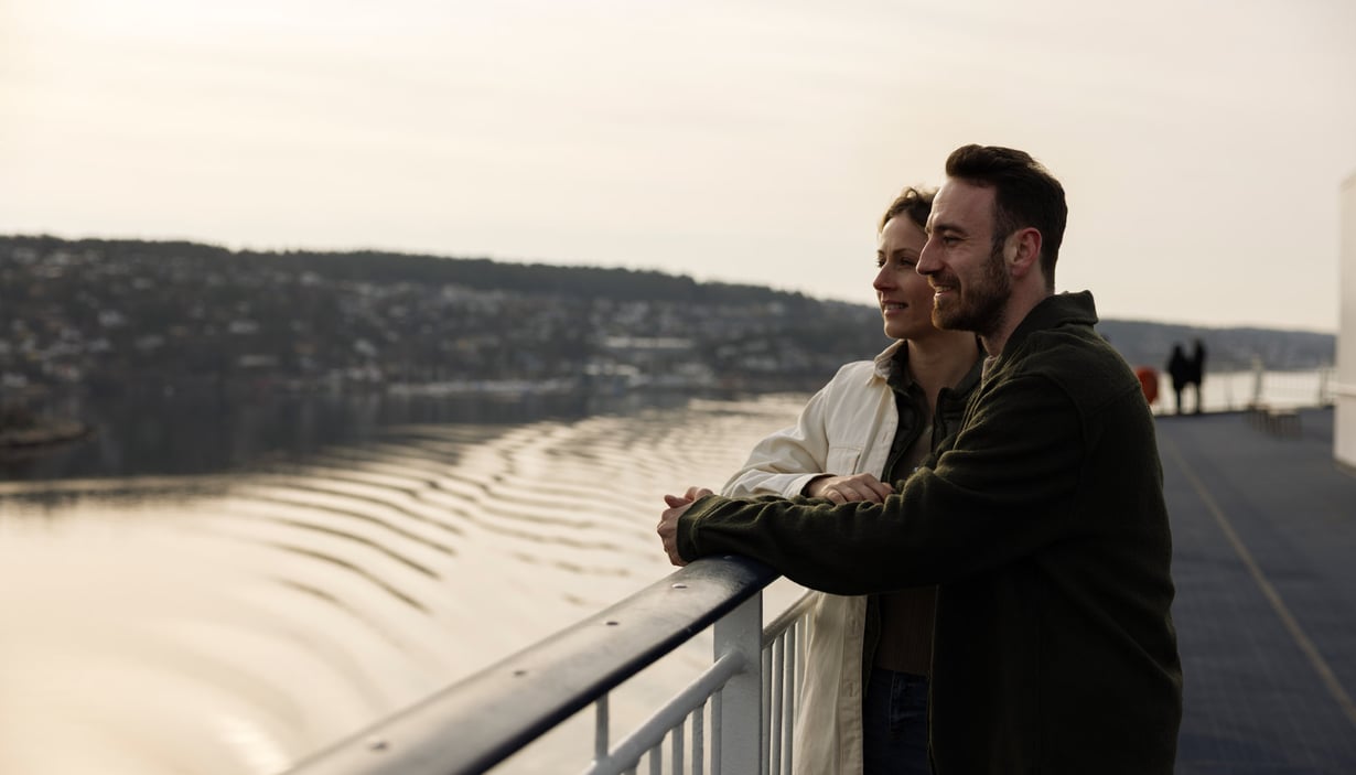 To personer står på et dæk og kigger ud over en vandmasse.