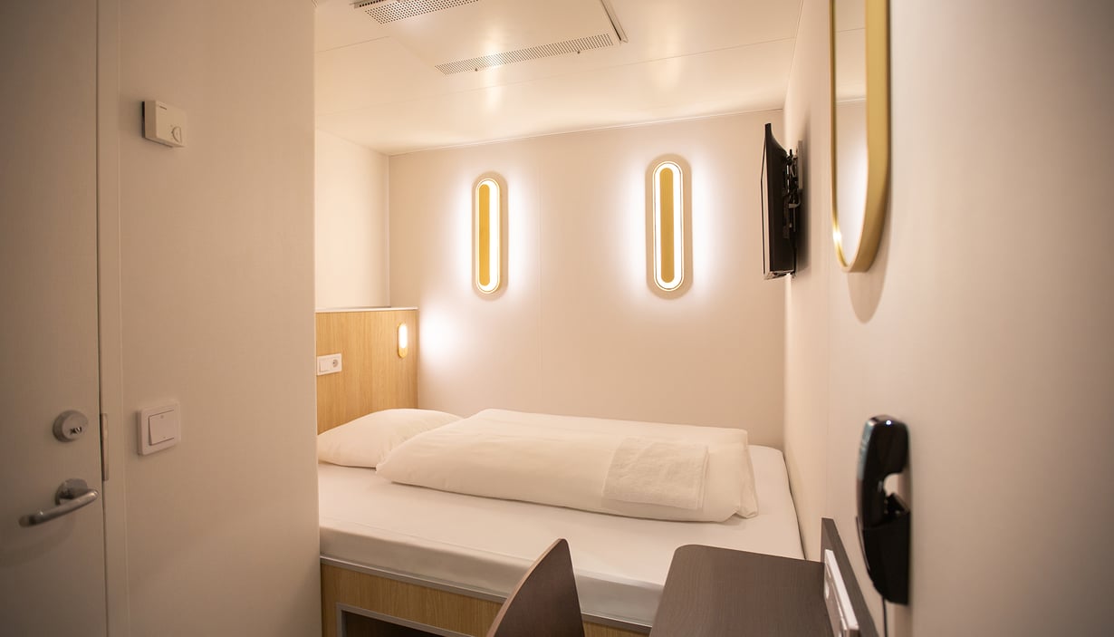 Moderne kahyt med enkeltseng, vægmonterede lys og TV.