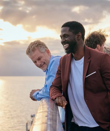 Fire personer, der står på en terrasse med havet og solnedgang i baggrunden.