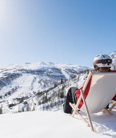 To personer sidder i liggestole på en sneklædt bakke i Hemsedal.