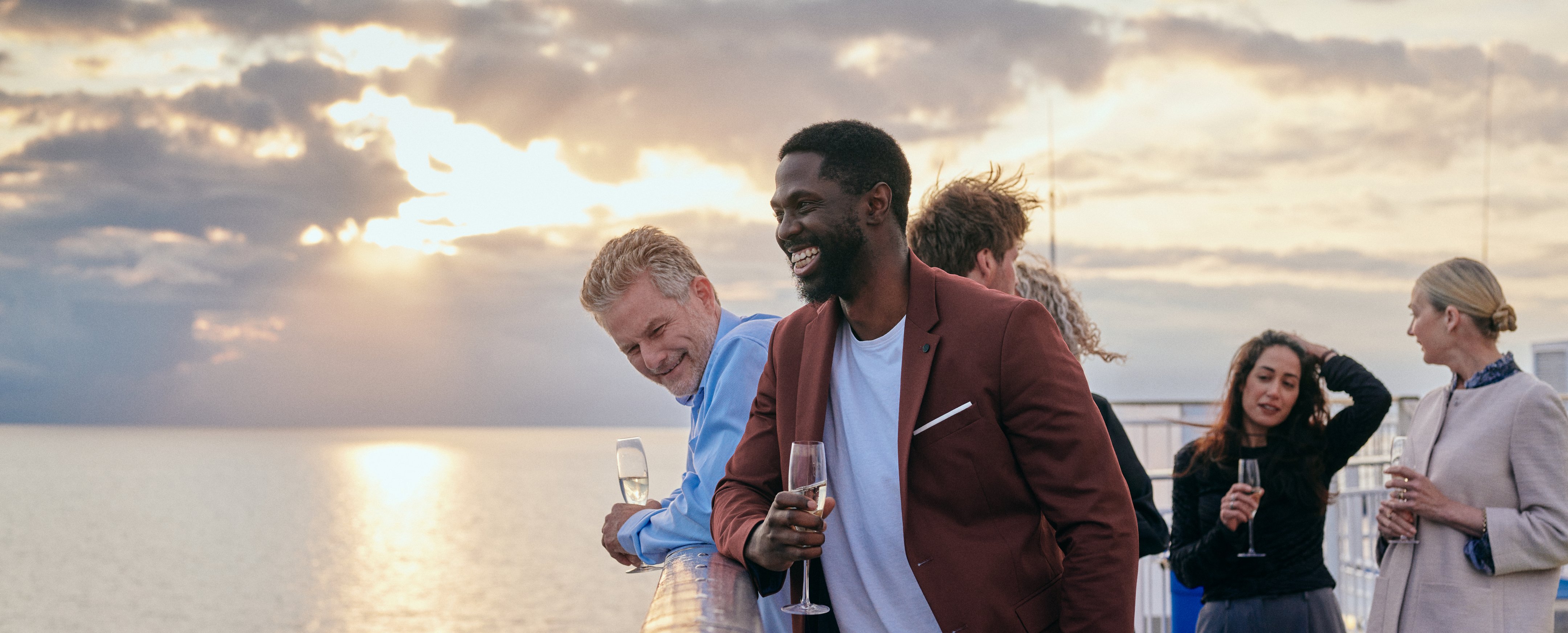 Gruppe af personer på en båd, der nyder havudsigten ved solnedgang med drikke i hånden