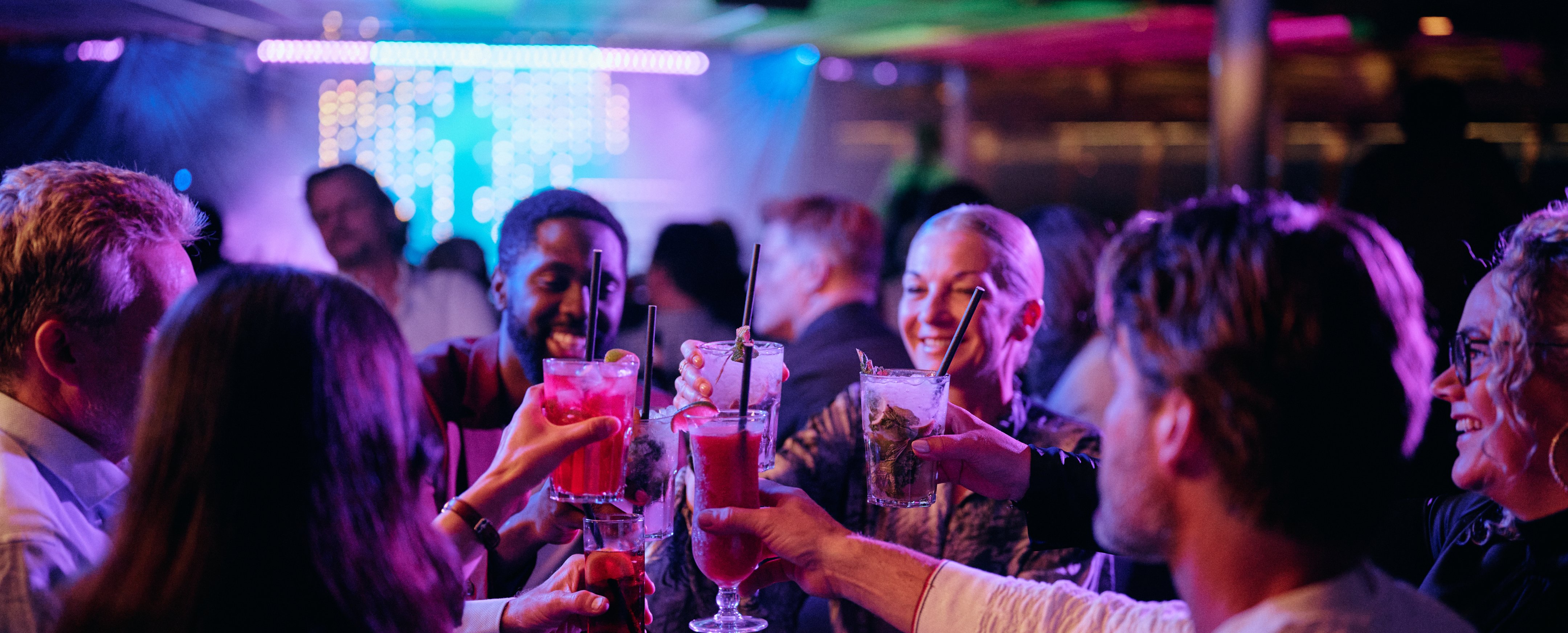 Folk fejrer på en livlig natklub med farverige lys og hævede glas