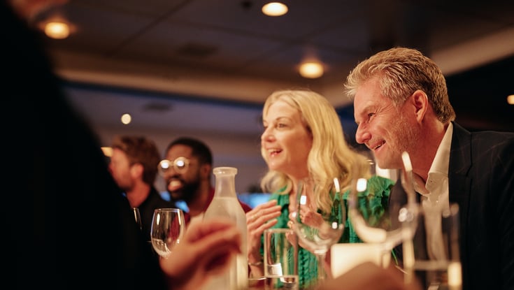 Venner samlet rundt om et restaurantbord med vin og vand, nyder en hyggelig aften indendørs