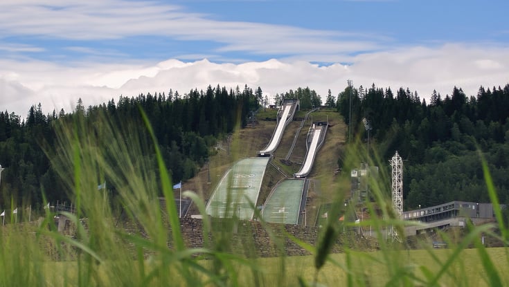 Skihopbakker i Lillehammer set gennem højt græs.