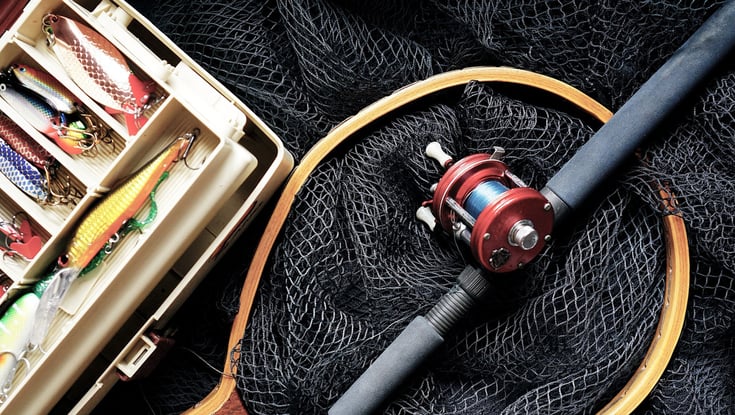 Fiskestang med hjul, fiskenet og åben grejboks med lokkemad.