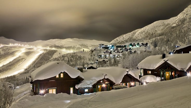 Snedækket bjerglandsby om natten med oplyste hytter.