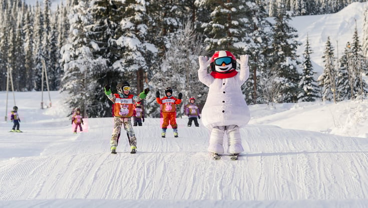 Person i en snemandkostume med skiløbere i baggrunden.