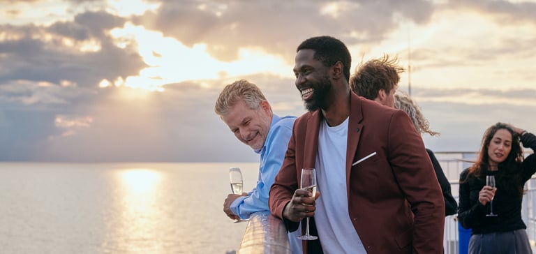 Gruppe af mennesker, der står på en båddæk med havet og solnedgang i baggrunden.