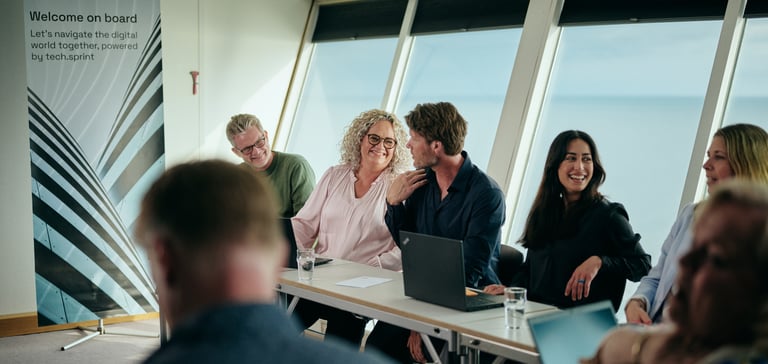 Møde med laptops ved vandudsigt, banner: "Welcome on board..."