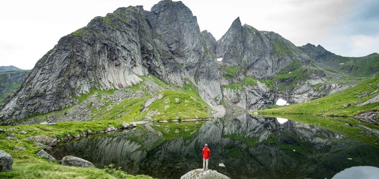 Person i rød jakke ved en rolig sø med grønne bjerge