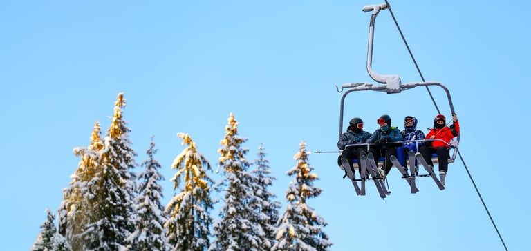 Gruppe af mennesker på en skilift med sneklædte træer i baggrunden.