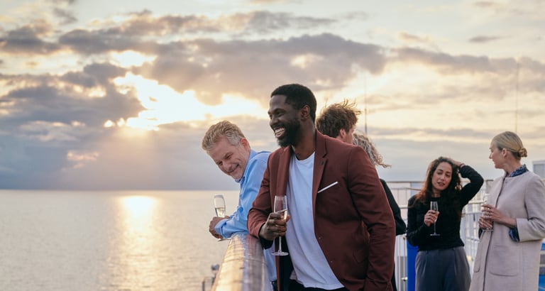 Gruppe af personer på en båd, der nyder havudsigten ved solnedgang med drikke i hånden