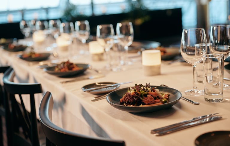 Elegant dækket spisebord med hvid dug, salater, bestik, stearinlys og vinglas