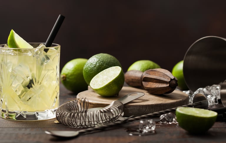 Cocktailglas med en drink og limekile omgivet af bartilbehør.