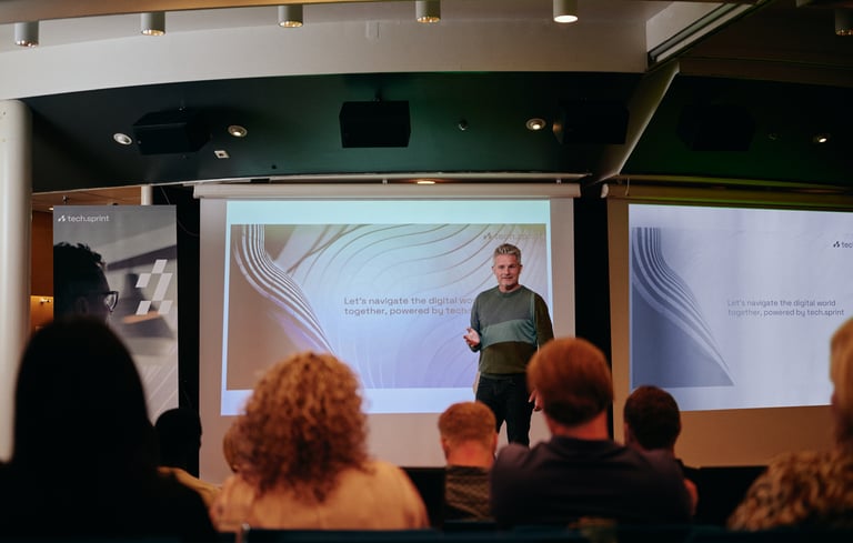 Person der giver en præsentation foran en skærm med publikum siddende.