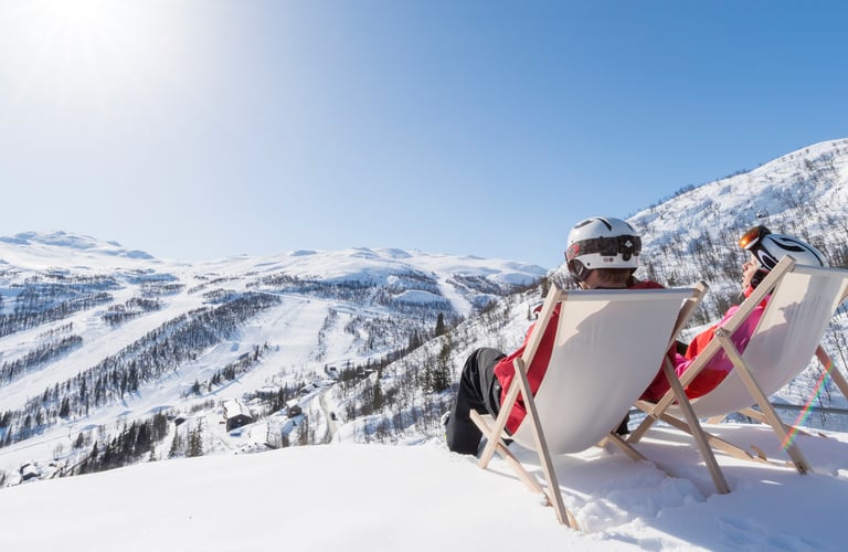 To personer sidder i liggestole på en sneklædt bakke i Hemsedal.